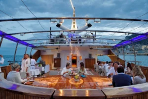 People on deck onboard Luxury yacht charter Christina O, famous for Onassis, Kennedy, Marilyn Monroe, Winston Churchill Library, celebrity charters, and featured in the movie 'Triangle of Sadness'
