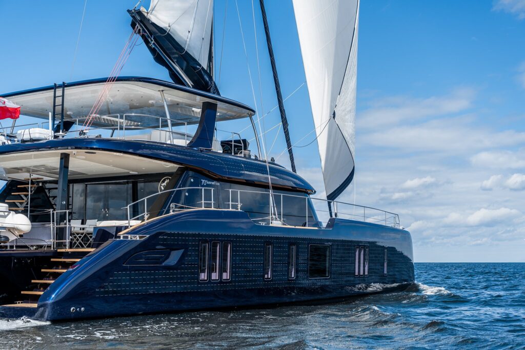 Sunreef Eco 70 catamaran ONE PLANET under sail, navy hull, seen from the water