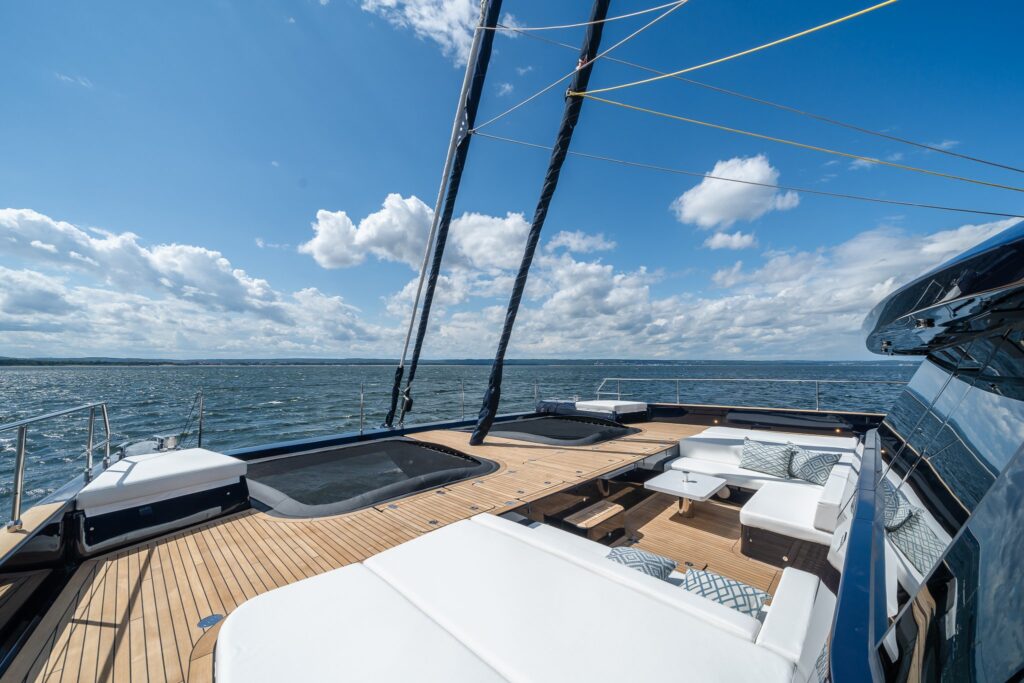 The teak foredeck of catamaran ONE PLANET with sunbeds and a lounge between the trampolines