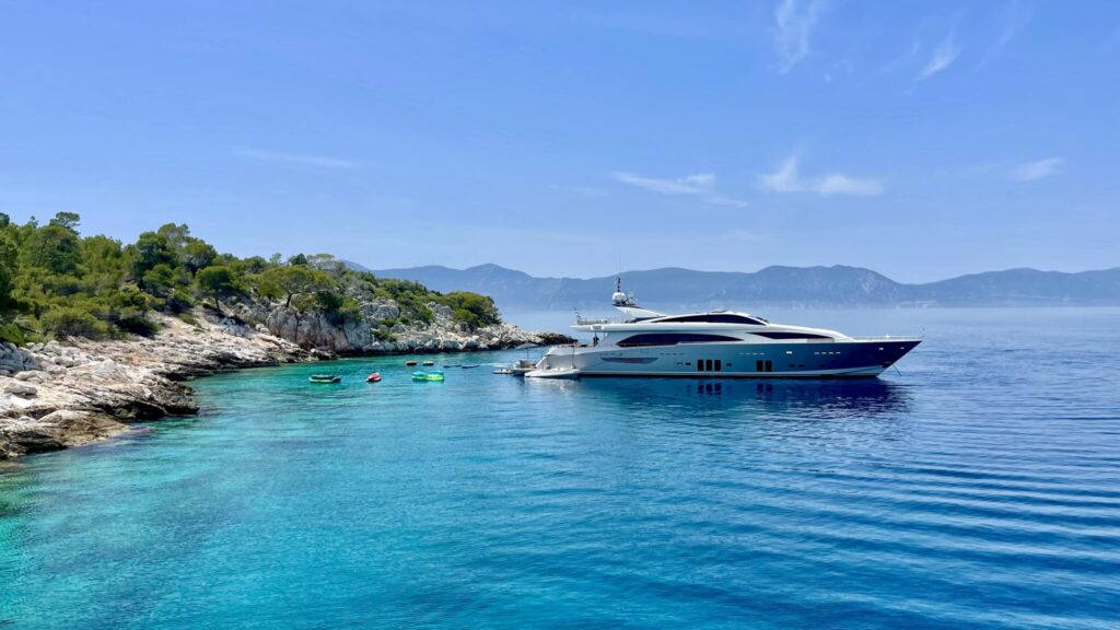 Motor yacht anchored stern-to in a sheltered pine-fringed cove in Greece