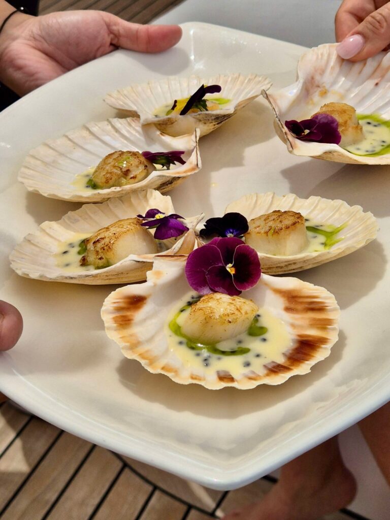 M/Y MILOS AT SEA serves Scallops in Shell Perfectly seared scallops in their natural shells, finished with a light citrus butter and edible flowers—almost too pretty to eat.