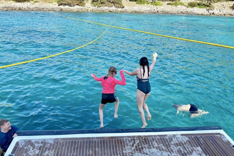 Children jumping from a yacht swim platform into the water.