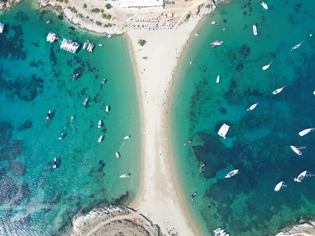 Aerial view of Kolona Beach on Kythnos, a narrow double-sided sandy isthmus with yachts anchored in turquoise water on both sides