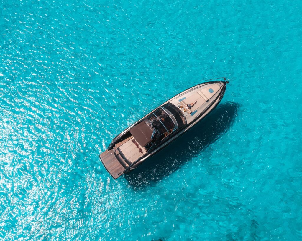 Top-down aerial view of a motor yacht anchored in crystal-clear turquoise water in the Cyclades