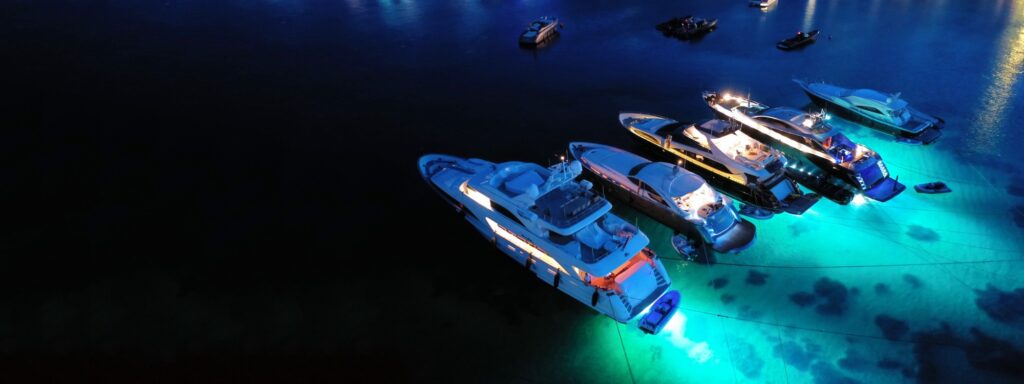 Aerial drone shot at night of motor yachts anchored off Psarou beach, Mykonos, with underwater lights on