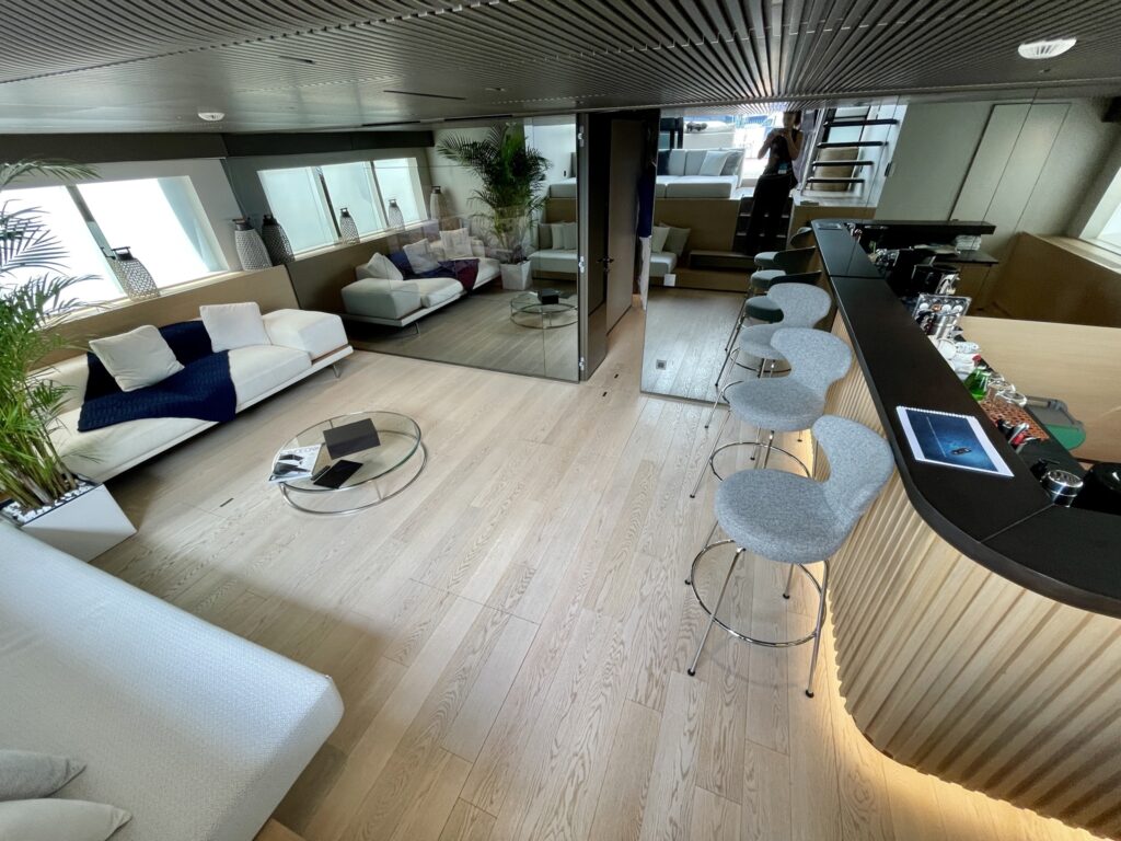 The open lounge and bar on the main deck of motor yacht BESTIA, with sofas, bar stools and large windows, May 2026.