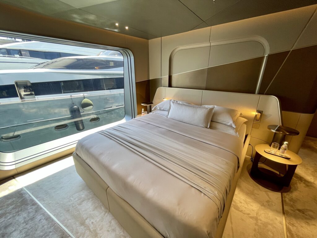 Double bed under a wide hull window in a guest cabin on THIS IS IT