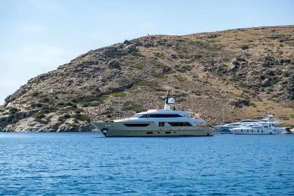 Yachts luxury motorboats moored at a secluded Kythnos island beach, Greece. Rocky hill, blue sea and sky background, sunny summer day.-min.