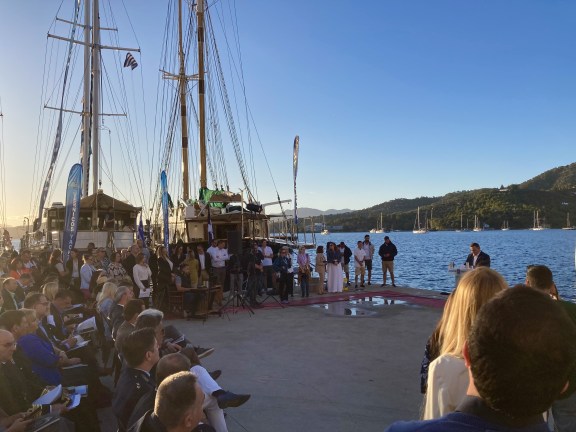 Lots of people gathered on the dock in front of 2 classic sailing yachts for the Official Opening Ceremony at the 2024 East Mediterranean Multihull Yacht Show (EMMYS) in Poros, Greece