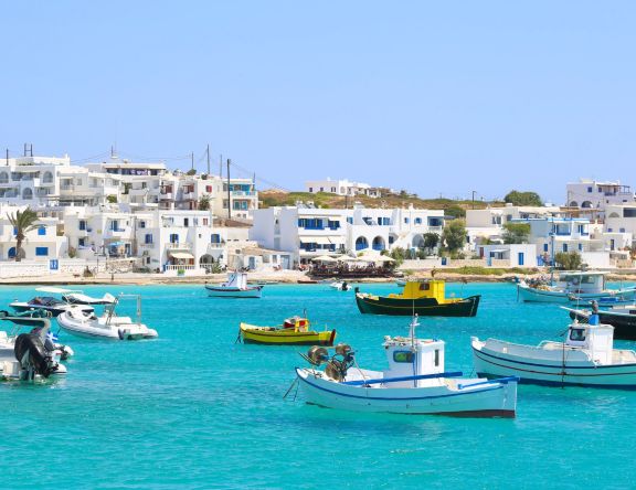 Small local fishing boats anchored off Ano Koufonisi in turquoise water, with white houses ashore.