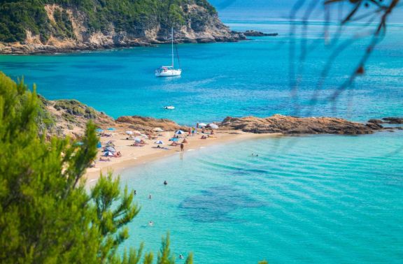 Poeple sunbathing at Little Banana Beach, Skiathos with a yacht anchored in the bay behind