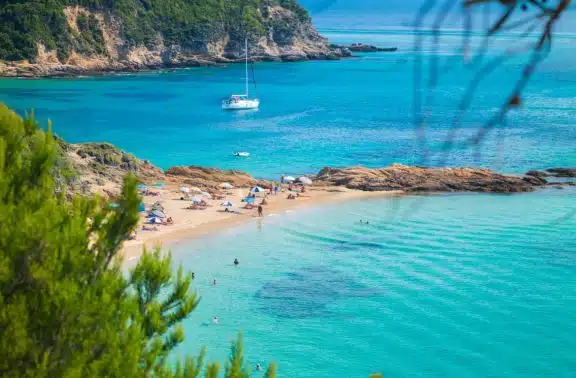 Poeple sunbathing at Little Banana Beach, Skiathos with a yacht anchored in the bay behind