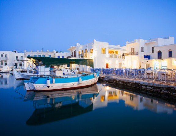 Naxos Greece restaurant right at the water in evening light with a small local boat moored of the wall