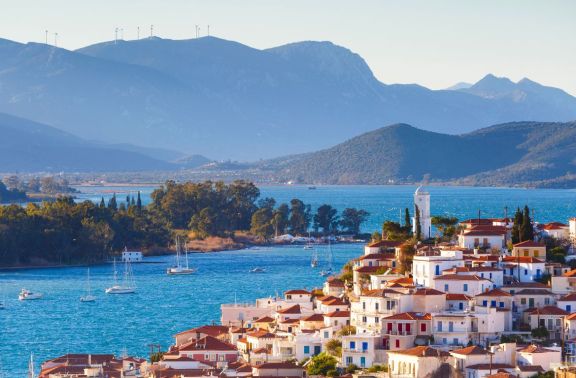 View over the town on Poros, over the bay with sailing yachts, and a backdrop of the mountainous shores of the Peloponnese Peninsula in the background.