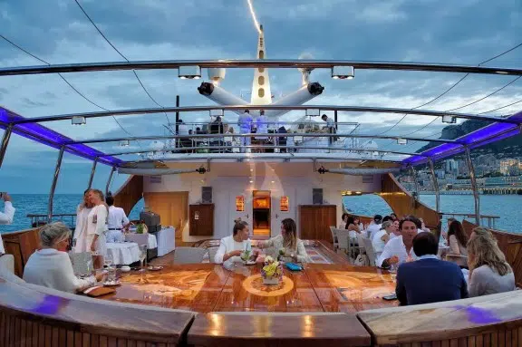 People on deck onboard Luxury yacht charter Christina O, famous for Onassis, Kennedy, Marilyn Monroe, Winston Churchill Library, celebrity charters, and featured in the movie 'Triangle of Sadness'