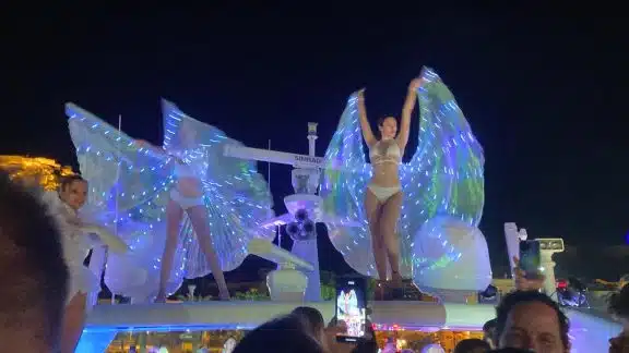 Performers in illuminated wing costumes on an outdoor stage at night.