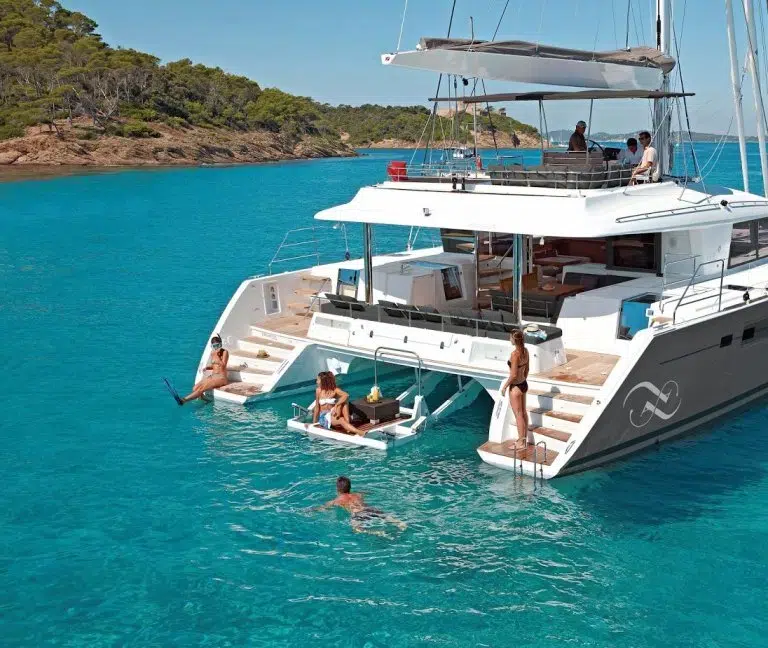 Charter guests swimming off swim platform of anchored catamaran in Greece