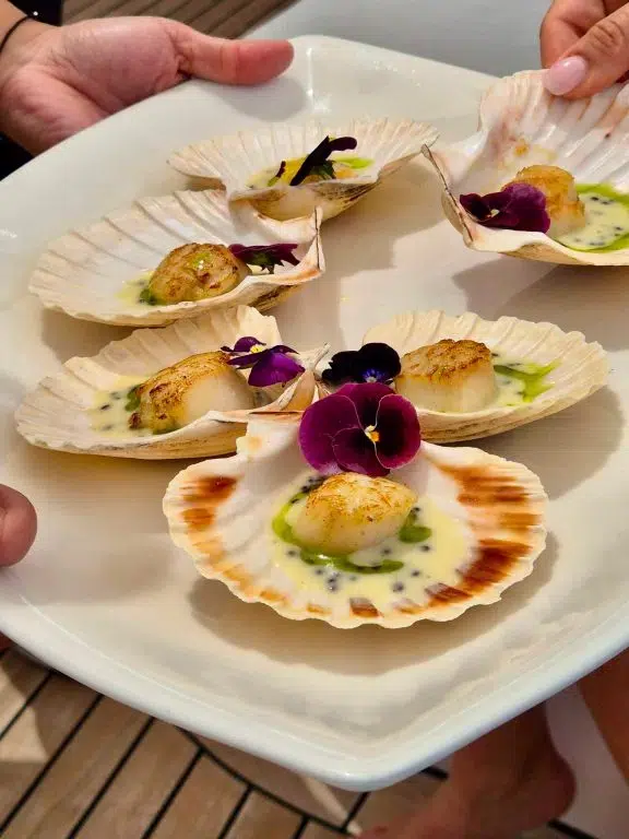 M/Y MILOS AT SEA serves Scallops in Shell Perfectly seared scallops in their natural shells, finished with a light citrus butter and edible flowers—almost too pretty to eat.