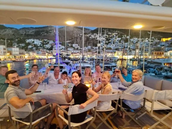 Group of people enjoying dinner on yacht overlooking Hydra town at night.
