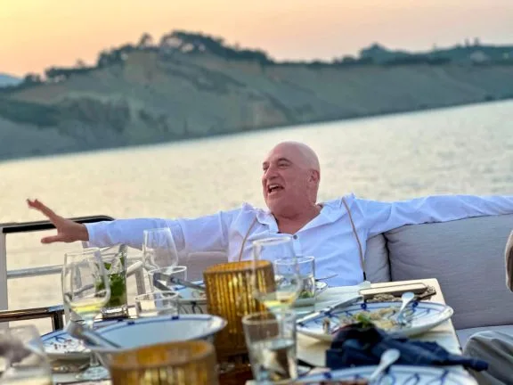 Man enjoying dinner on yacht deck with sunset view in background.